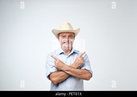 Votre publicité ici. Studio portrait of handsome man in blue shirt and cowboy hat montrant copie espace sur le mur. Heureux montrant américains âgés Banque D'Images
