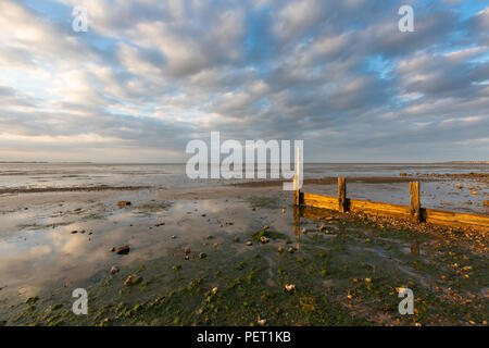 Belle lumière dorée juste avant le coucher du Soleil reflété sur une mer en bois plus une défense ciel dramatique, Seasalter, Whitstable, Kent, UK sur la côte nord du Kent. Banque D'Images