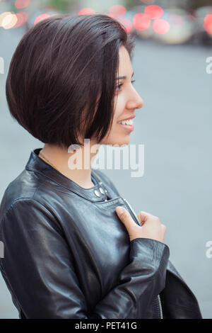 Closeup portrait of beautiful smiling young hispanic latin fille femme avec de courts cheveux noir foncé, bob porter veste en cuir, extérieur à l'écart, et Banque D'Images