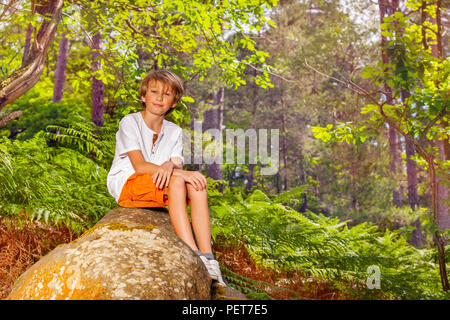 Portrait de l'âge scolaire garçon s'asseoir sur le rocher dans la forêt pendant la randonnée Banque D'Images