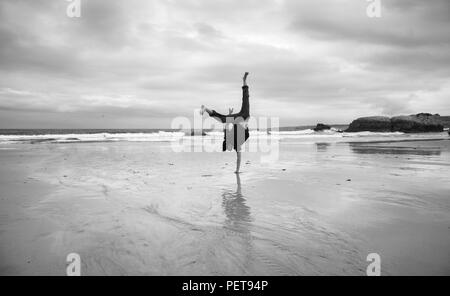 Jeune homme sur une plage de sable humide faisant l'acrobatie, l'image monochrome Banque D'Images