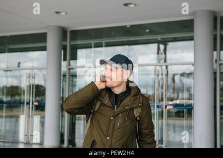 Un jeune homme à l'aéroport touristique ou près d'un centre commercial ou un poste, un taxi ou les discussions sur un téléphone cellulaire ou communique avec des amis à l'aide d'un téléphone mobile. Banque D'Images