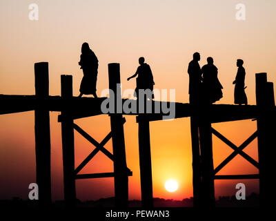 Vue paysage de la U Bein (U-Bein) bridge près de Amarapura au Myanmar au coucher du soleil, avec les habitants de silhouette noire et des moines de marcher sur le pont Banque D'Images