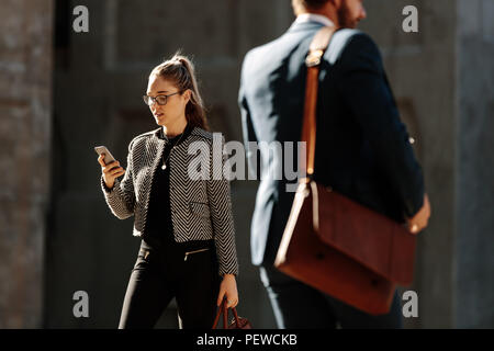 Businesswoman se rendre au bureau le matin en regardant son téléphone portable. Business people walking on city street à leur bureau comptable bureau b Banque D'Images