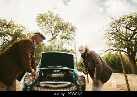 Laughing couple debout devant leur voiture cassée avec ouvrir le capot. Vieil Homme et femme sur la date avec voiture cassée. Banque D'Images