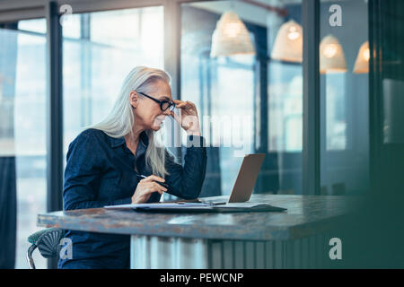 Senior business woman working on laptop in office. Femelle mature woman looking at laptop computer en étant assis à son bureau.