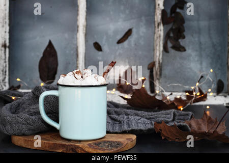 L'émail bleu et noir tasse de chocolat chaud avec des guimauves et écorce de cannelle en face d'une ancienne fenêtre. L'extrême profondeur de champ avec l'accent sur dri Banque D'Images