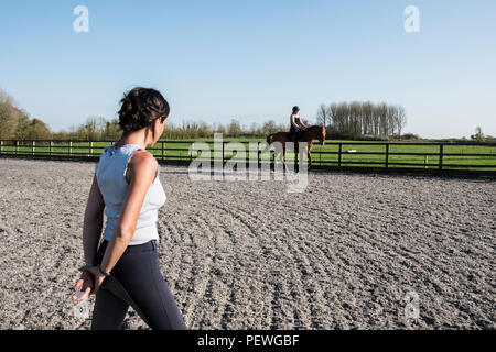 Formateur Femme regardant une adolescente à cheval sur un baybrown cheval en paddock. Banque D'Images