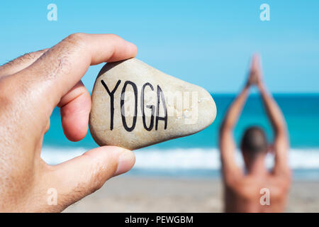 Libre de la main d'un jeune homme de race blanche sur la plage tenant une pierre avec l'yoga écrit en C, et d'un young caucasian man practicing yoga in th Banque D'Images