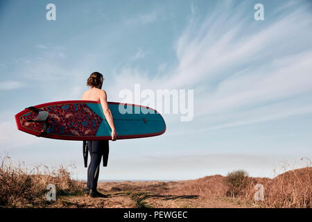 Homme marchant sur un chemin dans les dunes de sable de la mer vers la réalisation d'une planche de surf. Banque D'Images