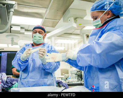 Le 96e Escadron d'opérations médicales Jesse Aguilar, technicien de laboratoire d'un cathéter et Senior Airman Samantha Bautista, un technicien cardiopulmonaires, suivez les procédures d'enfiler des gants stériles à l'Hôpital d'Eglin, 14 janvier à la base aérienne d'Eglin, en Floride, les techniciens chirurgicaux disposés à aider les médecins au cours d'un cathétérisme cardiaque. Le plus récent d'Eglin procédure d'imagerie invasive permet aux médecins d'identifier la façon dont le sang d'un patient s'écoule vers l'artère qui irrigue le cœur. (U.S. Air Force photo/Ilka Cole) Banque D'Images