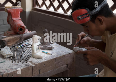 Un sculpteur cambodgien sculpte soigneusement un Bouddha en pierre dans un centre d'art de Siem Reap, reflétant l'artisanat traditionnel et la vie quotidienne en Asie. Banque D'Images