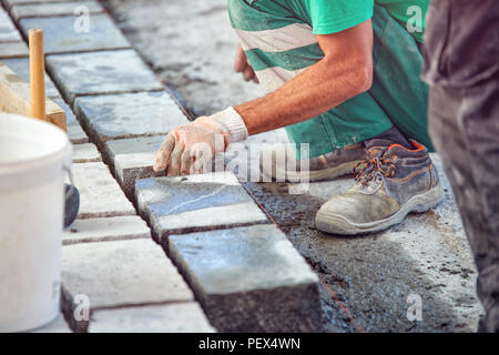 Un ouvrier a les mains gantées utiliser un marteau pour placer les pavés en pierre. La création d'un travailleur à l'aide de blocs et de la chaussée pavée de pierres de granit. Je travailleur industriel Banque D'Images