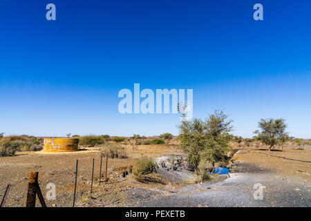 Un réservoir d'eau et moulin à vent debout dans un paysage désolé et à distance sur une ferme rurale en Namibie. Banque D'Images