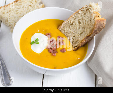 Butterrnut et bacon soupe garnie de crème sure, lardons et scallon pain ciabatta avec close up sur le tableau blanc rustique haut Banque D'Images