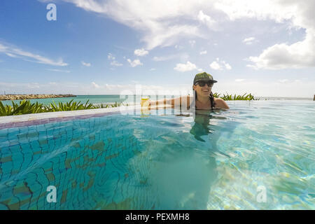 Woman swimming in oceanside piscine avec cocktail Banque D'Images