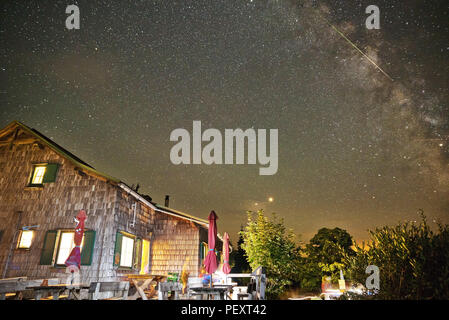 Chalet de montagne en Autriche dans la nuit avec un ciel étoilé montrant Voie lactée et les étoiles filantes des Perséides, ainsi que des planètes Mars et Saturne. Banque D'Images