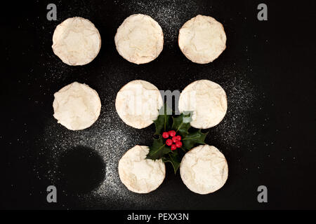 Délicieux mince pies de Noël fraîchement cuits au four avec un manque, avec Holly berry branche feuilles et sucre glace Poussière sur fond noir. Vue d'en haut. Banque D'Images