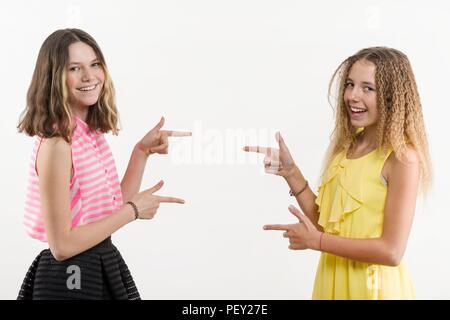 Deux adolescentes positifs attrayants pointant son index à l'écart, indiquant l'espace de copie sur mur blanc vide de votre contenu ou de promotion d'informer Banque D'Images