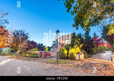 Route asphaltée dans la rue de l'automne d'arbres et de feuilles tombées, maison d'habitation, clôture verte à partir de plantes, de barrières, ciel bleu Banque D'Images