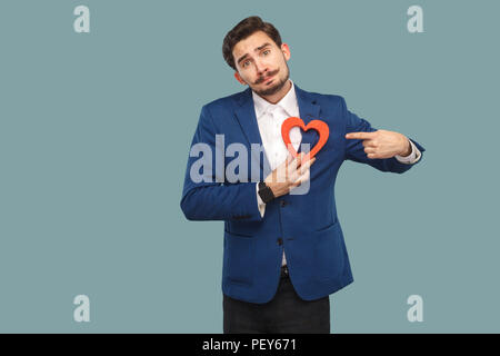 Triste Malheureux cœur brisé l'homme à veste bleue et chemise blanche, debout et tenant en forme de coeur rouge et à la caméra et au doigt. Piscine, s Banque D'Images