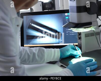 Médecin légiste à l'aide d'un microscope stéréo 3D pour voir les marques sur une balle dans le laboratoire au cours d'une enquête criminelle. Banque D'Images