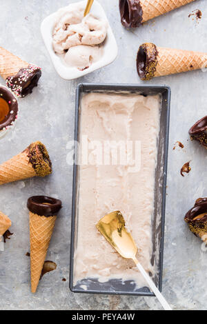 Glace à la banane sur un conteneur métallique, avec les cônes ith ganache chocolat faits pour les décorer, vue du dessus composition contre un carton gris. Banque D'Images