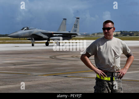 Les cadres supérieurs de l'US Air Force Airman Joshua Miller, chef d'équipe affectée au 112e Escadron de chasse de l'expéditionnaire, se dresse sur la ligne de vol à Andersen Air Force Base, Guam, qu'un F-15 Strike Eagle taxis derrière lui le 15 février 2016, au cours de l'effort à faire face au nord en 2016. Exercices de formation tels que le CN16, les États-Unis, le Japon et l'Australie, les forces de l'air développer les capacités de combat, l'amélioration de la supériorité aérienne, la guerre électronique, de l'interdiction aérienne, le transport aérien tactique et aerial refueling. (U.S. Photo de la Garde nationale aérienne par le sergent. Shane Hughes/libérés) Banque D'Images