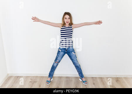 Jeune fille 11 ans avec de longs cheveux blonds, debout près de mur blanc et les mains sur les côtés Banque D'Images