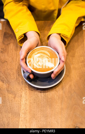 Les mains tenant une latte sur une table en bois. Banque D'Images
