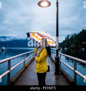 Jeune femme dans un imperméable jaune permanent, sous un parapluie un jour de pluie par l'océan. Banque D'Images