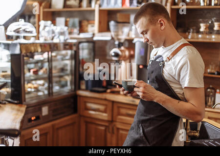 Handsome bartender de boire du café et texting message dans le concept de communication smart phone. Banque D'Images