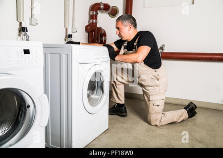Plombier en uniforme les réparations à l'intérieur de lave-linge dans la blanchisserie Banque D'Images