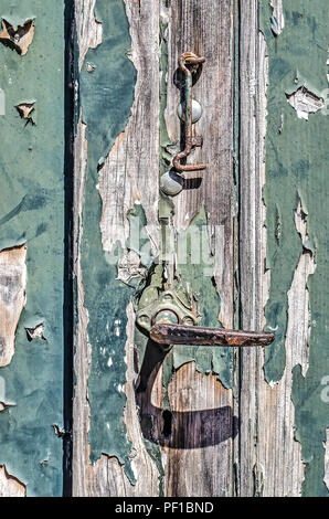 Close-up d'un bouton de porte en acier rouillé et crochet sur une porte en bois patiné avec peeling peinture verte Banque D'Images