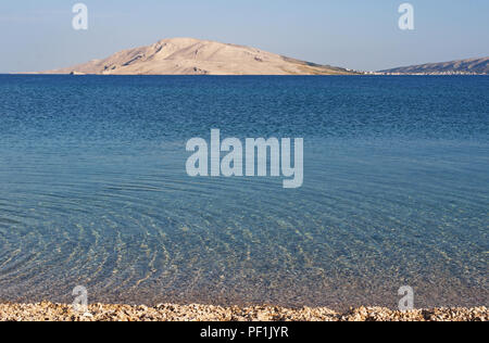 Croatie : l'eau cristalline de Rucica, la plage de galets située dans une baie aride entourée par un paysage désertique sur la célèbre île de Pag Banque D'Images