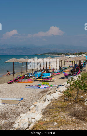 Chaises longues, transats en rotin et osier ou nuances soleil tropical et des parasols sur une plage de sable sur l'île grecque de Corfou en Grèce. Banque D'Images