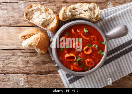 La nourriture italienne maison squid braisé en sauce tomate avec des épices et persil close-up dans un pot, et de pain frais. Haut horizontale Vue de dessus Banque D'Images