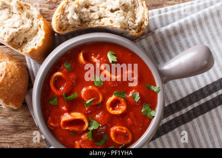 Fruits de mer méditerranéens traditionnels anneaux de calmars de la tomate avec des épices et persil close-up dans un pot et de pain frais. Haut horizontale Vue de dessus Banque D'Images