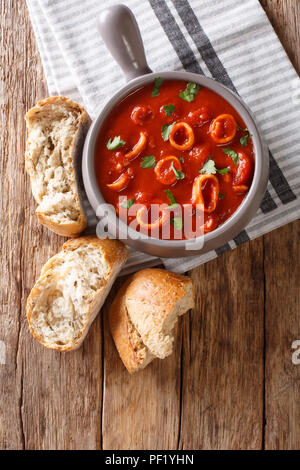 La nourriture italienne maison squid braisé en sauce tomate avec des épices et persil close-up dans un pot, et de pain frais. vertical haut Vue de dessus Banque D'Images