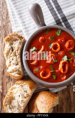 Fruits de mer méditerranéens traditionnels anneaux de calmars de la tomate avec des épices et persil close-up dans un pot et de pain frais. vertical haut Vue de dessus Banque D'Images