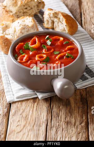 De délicieux anneaux de calmars de la tomate avec des épices et persil close-up dans une casserole, avec du pain. vertical Banque D'Images