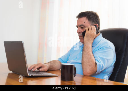 Angry Man working on laptop tout en parlant au téléphone. L'émotion négative. Banque D'Images