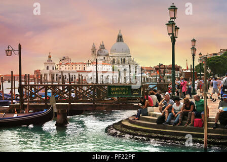 Venise, Italie, Juin 8, 2018 : les touristes assis sur les marches près de gondoles avec Basilica di Santa Maria della Salute en arrière-plan Banque D'Images