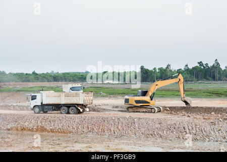 La charge de la machine excavatrice jaune sol dans un camion-benne at construction site Banque D'Images
