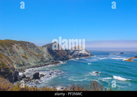 Vue vers l'Ouest sur une magnifique baie avec une mer d'Azur et le ciel bleu clair, tipped vagues s'écraser sur les rochers escarpés entourant la baie. Banque D'Images