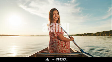 Jeune femme à l'arrière par-dessus son épaule tout en canoë sur un lac sur une après-midi ensoleillée en été Banque D'Images