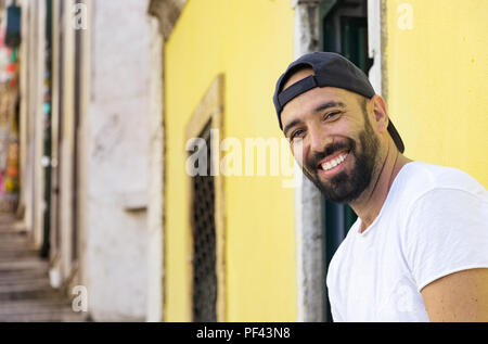 Portrait d'un homme espagnol avec sourire à la caméra, barbe portant un chapeau snapback et un t-shirt, à l'extérieur. Banque D'Images