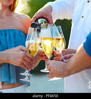 Happy friends pouring champagne vin mousseux dans des verres en plein air sur une plage. Sunset beach party Banque D'Images