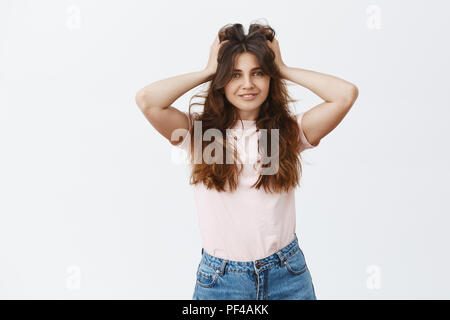 Tourné à l'intérieur de l'heureux et insouciant femme sentiment satisfait après avoir portant révision de coiffure en masque capillaire incroyable toucher moelleux et belle coiffure tout sourire sur fond gris Banque D'Images