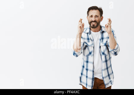 Guy nerveuse intense priant son dieu se passera bien. Portrait of mature anxieux caucasian man with beard, fronçant les sourcils et serrant les dents, tout en traversant les doigts et faire souhaiter bonne chance Banque D'Images